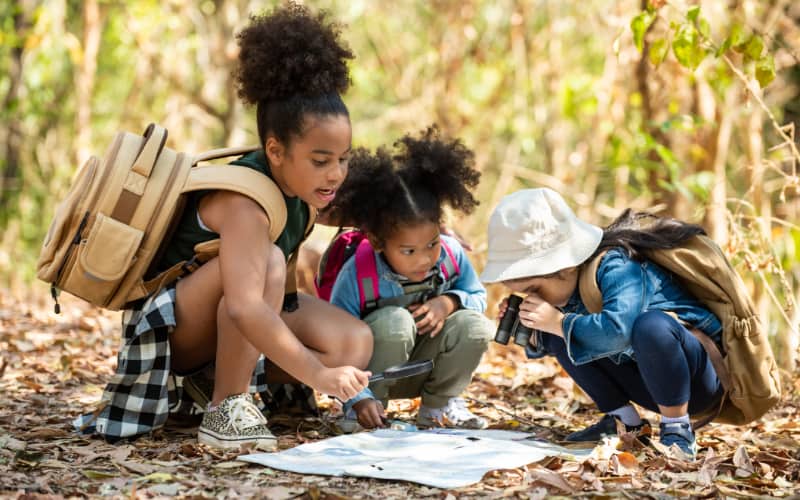 Three young children in the woods looking at a map