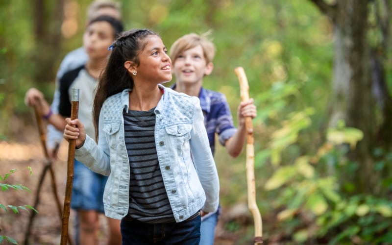 A group of teens with walking sticks hike through the woods